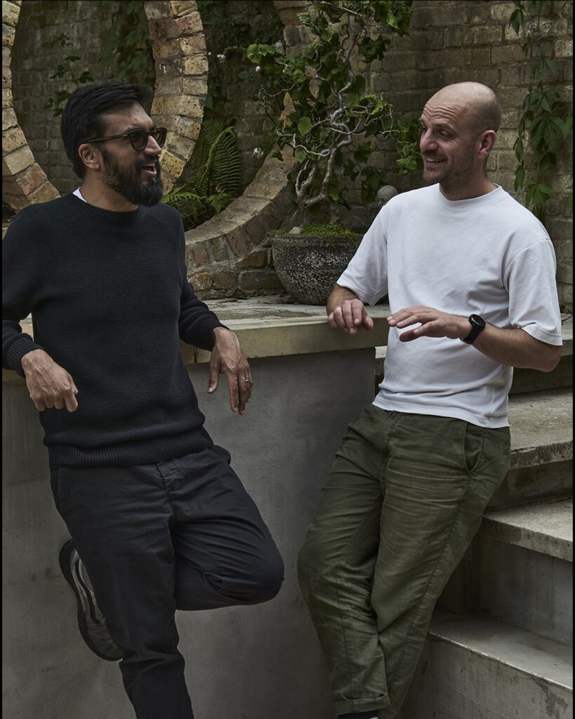 Roland and Dev in conversation in front of crescent-shaped-brick-wall